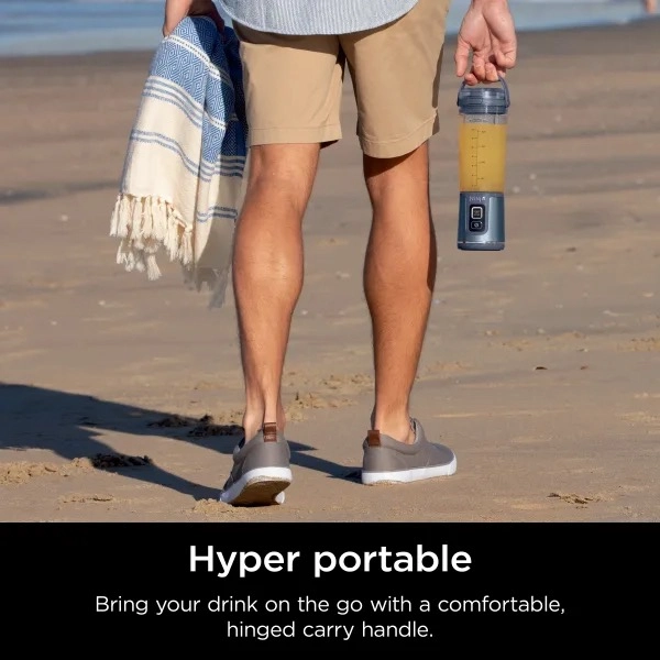 photo of a person holding a ninja blast portable blender walking on the beach